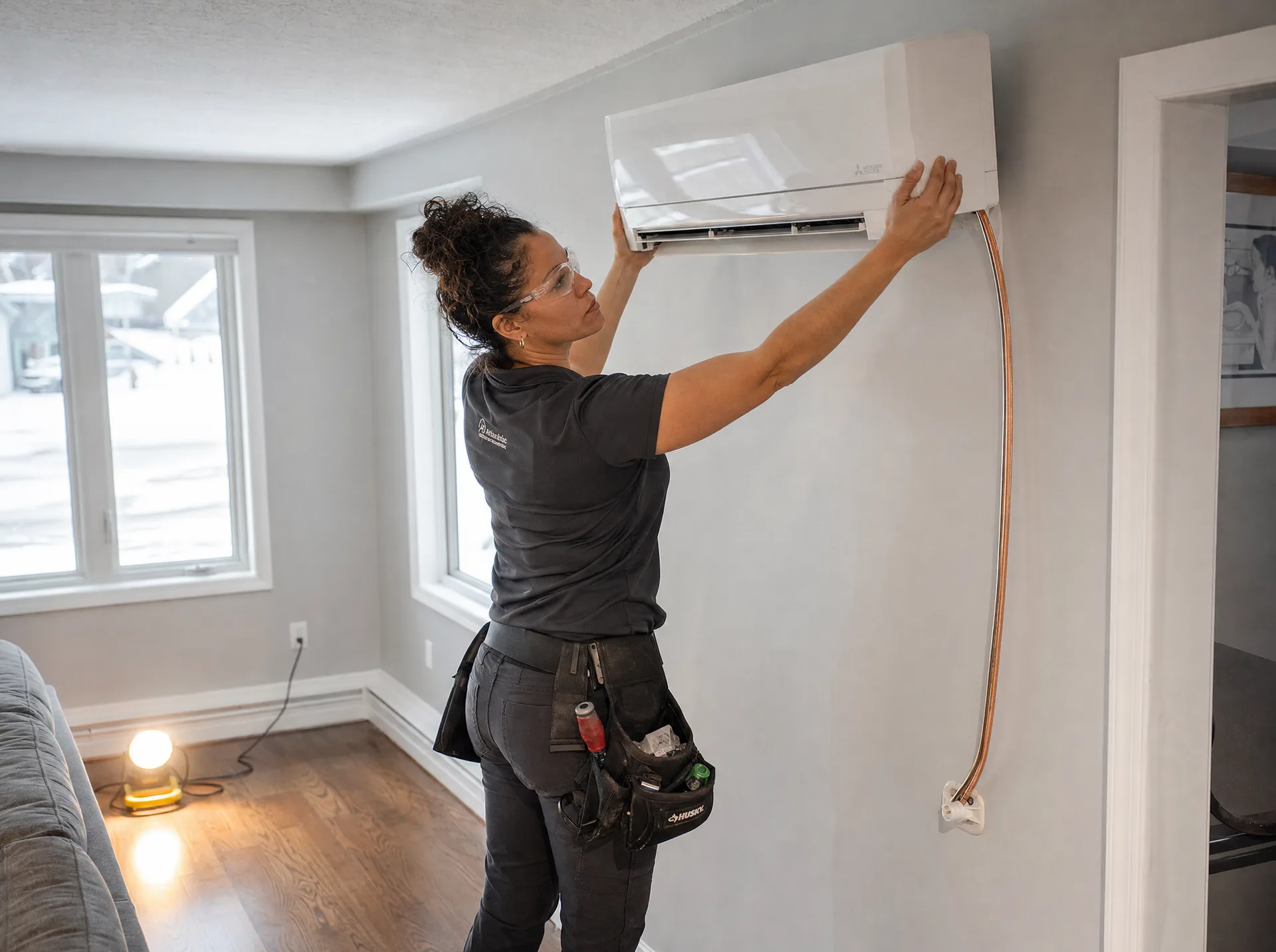 HVAC installer mounting a ductless mini-split indoor head on the wall of a Canadian living room